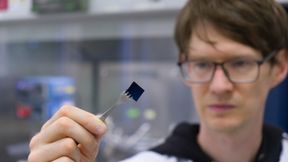Stefan Schröder hält eine mit einer hauchdünnen Polymerbeschichtung versehene Siliziumprobe. Die Beschichtung ist mit bloßem Auge nicht sichtbar. (Bild: Christina Anders, Uni Kiel)
