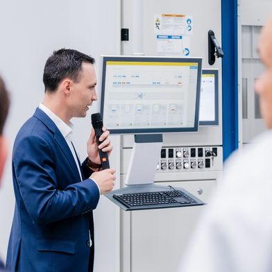 Benedikt Gundling demonstriert das Auftragsmanagement vom Cosera vor einem Bearbeitungszentrum. Der Bestand des Palettenmagazins wird ebenfalls angezeigt. (Bild: Grob/Coscom)