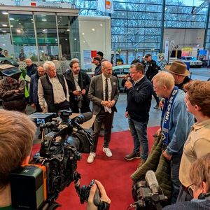 Classic-Bremen-Motorshow-Cheforganisator Frank Ruge (grauer Anzug) interviewt die beiden Gäste John Wheeler, Konstrukteur des Ford RS200 (li.) und Ernst Kopp, Rennmechaniker am Toyota 222D (am Mikro).(Bild:  Dominsky – VCG)