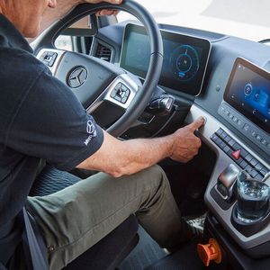 Der Mensch hinter dem Lenkrad des 19-Tonners blickt auf zwei Bildschirme, die das Geschehen rund um den Truck zeigen.(Bild:  Daimler Truck)