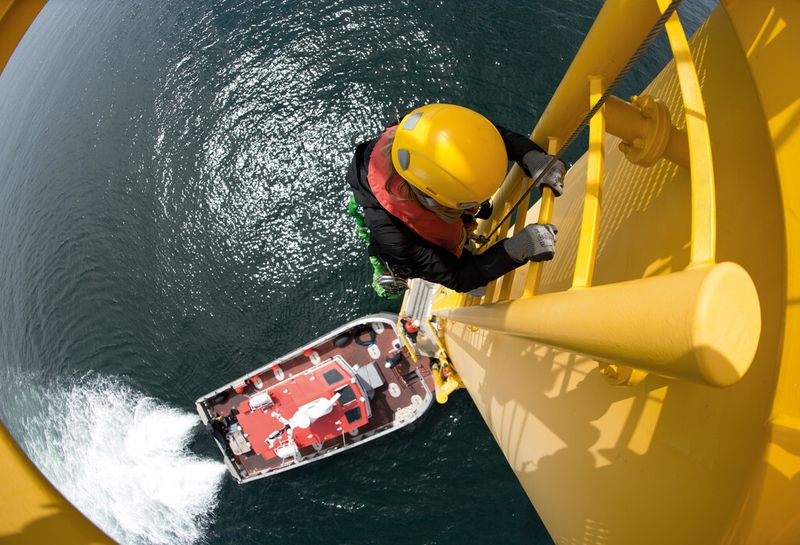 Obwohl ein in den Türmen der Windturbinen eingebauter Lift die Service-Techniker zumindest einen Teil der Wegstrecke bis zur Gondel hinauf transportieren kann, müssen nach wie vor Leitern benutzt werden. Auch hier werden besondere Sicherheitsstandards trainiert. Das Bild zeigt das Übersteigen eines Service-Technikers vom Boot auf das Übergangsstück zwischen Fundament und Turm der eigentlichen Windturbine im Offshore-Windkraftwerk Rhyl Flats in Großbritannien. (Bild: Siemens)