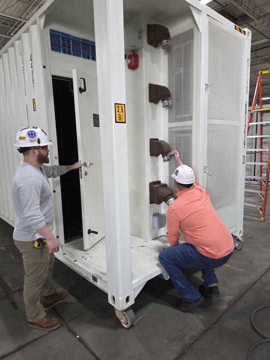 Korey Greene und John Salyers untersuchen die elektrischen Anschlüsse eines Containers, der für die Stromversorgung bei Arbeiten an transkontinentalen Unterwasserkabeln installiert wurde.(Bild:  Sea Box)
