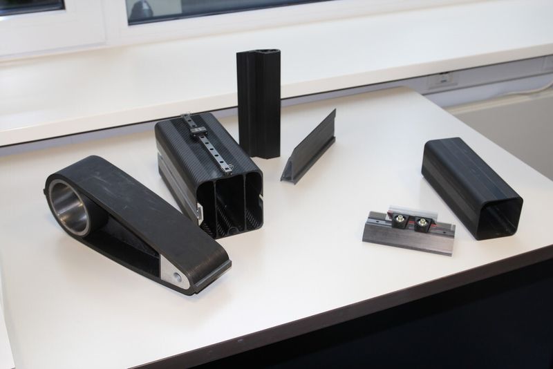 Beispiele für gelungene CFK-Maschinenelemente auf der VDMA-Tagung „Maschinenkomponenten aus Composites“, wie sie bei der Karl Mayer Textilmaschinen GmbH hergestellt werden: Ganz links ein Carbonhebel, diverse Profile, die unter anderem durch Schlauchblasen entstanden sind und das vorletzte Objekt ist ein sogenannter Barren für den Einsatz in Textilmaschinen. (Bild: Königsreuther)