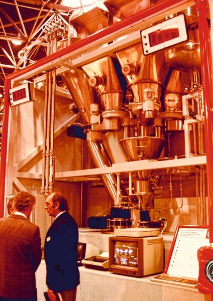 1979 sees the use of the first PLC, followed by a control system just a few years later — the start of production of fully-automated dosing container systems. The picture was taken at the plastics fair Kunststoffmesse 1983, where the production process was presented as a multicolor graphic for the first time.  (Azo)