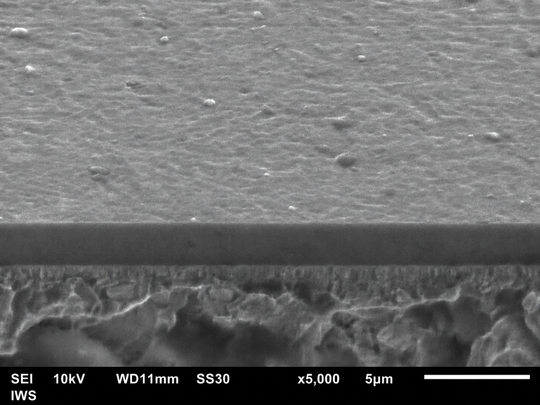 Mittels 90-Grad-Plasmafilterung hergestellte, etwa 2,5 µm dicke ta-C-Schicht. Schrägansicht auf die Bruchfläche im Rasterelektronenmikroskop. Die Partikelabtrennung des Fraunhofer IWS führt zu einer glatten, defektarmen Oberfläche und steigert die Lebensdauer belasteter Komponenten.(Bild:  Fraunhofer IWS)