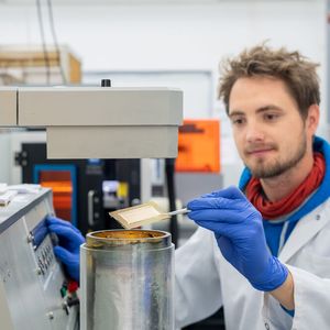 Doktorand Lukas Hiendlmeier beim Bearbeiten der Elektroden. Für die leitfähigen Strukturen wird unter Hochvakuum eine dünne Lage Gold auf das 3D gedruckte Substrat aufgebracht. Im Hintergrund: Lasersystem für die Strukturierung.(Bild:  Andreas Heddergott / TU München)