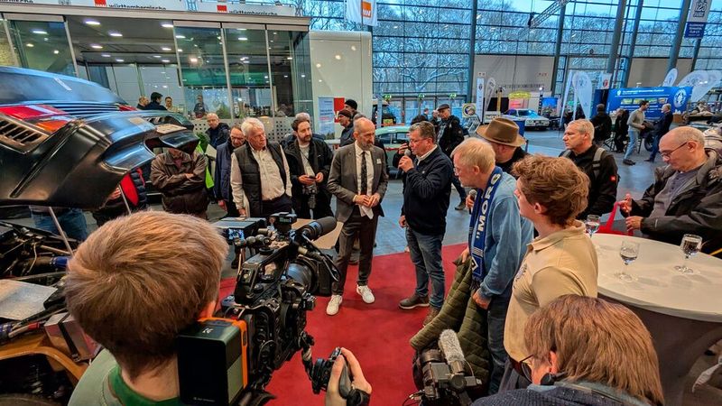 Classic-Bremen-Motorshow-Cheforganisator Frank Ruge (grauer Anzug) interviewt die beiden Gäste John Wheeler, Konstrukteur des Ford RS200 (li.) und Ernst Kopp, Rennmechaniker am Toyota 222D (am Mikro). (Bild: Dominsky – VCG)