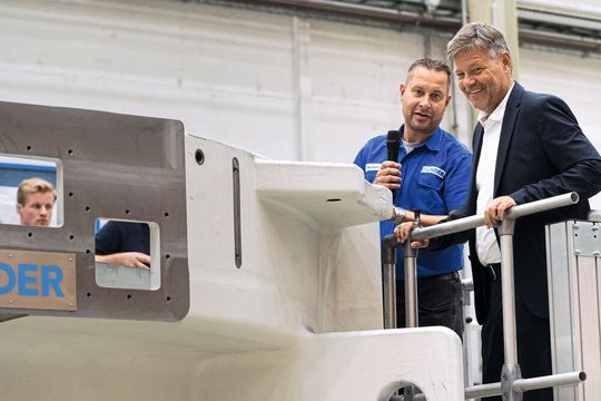 Montagemeister Benedikt Bauhaus erläutert Minister Habeck, wie in mehreren Metern Höhe die Zahnräder in das 120-Tonnen-schwere Getriebe einer Zementmühle eingesetzt werden.(Bild:  Flender GmbH)