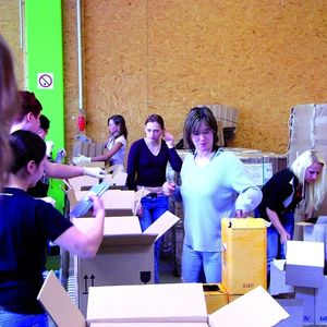 Während vorne am Transportband die Kartons mit Flaschen befüllt werden, ist dahinter das Team damit beschäftigt, die leeren Weinlieferkartons zu entsorgen und neue Kartons für die schnelle Flaschenentnahme zu öffnen.