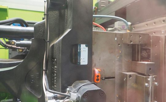 Geklebte Künstliche Intelligenz von Aisemo an der Spritzgießmaschine! Der Sensor muss nur an die auswerferseitige Aufspannplatte einer Spitzgussmaschine geklebt werden, schon liefert er kontinuierlich Informationen zu Temperatur und Bewegungen, was die Kunststoffteilefertigung produktiver macht. (Bild:  Aisemo)