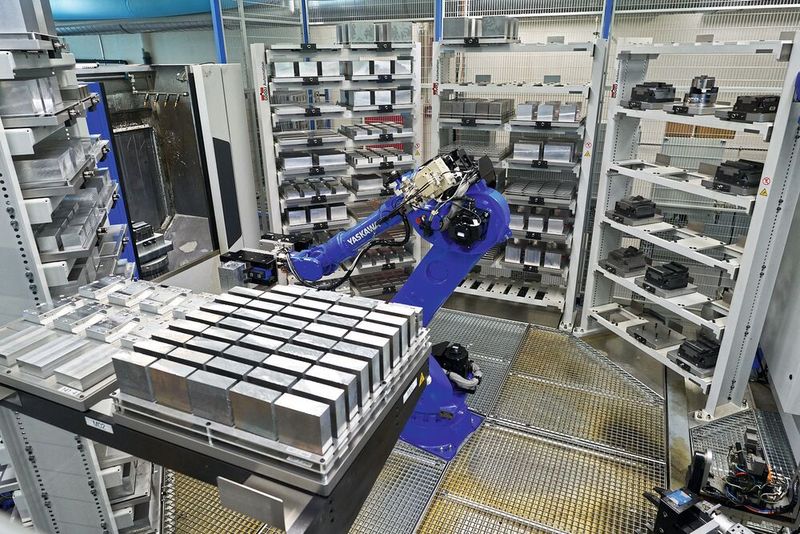 Blick in den Automationsbereich einer Fertigungsinsel mit zwei Heller «HF 3500». Gut zu erkennen sind die Paletten mit unterschiedlichen Roh- und Fertigteilen sowie der Knickarmroboter, der sowohl die Teile als auch die Paletten handeln kann. Im oberen Bild sind die beiden rückwärtigen Türen der Heller «HF 3500» zu erkennen, die über einen Schwenktisch verfügen und die Rohteile in den Bearbeitungsraum schwenken. Rechts unten sind darüber hinaus die verschiedenen Greifer für unterschiedliche Bauteile zu erkennen. (Bild: Eugen Seitz AG)