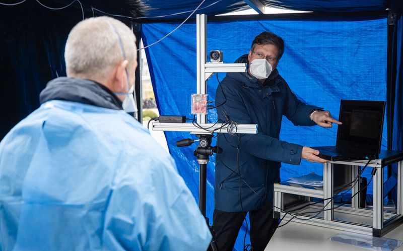 Dr. Urs Schneider vom Fraunhofer IPA erklärt die Messungsdurchführung. Der Mitarbeiter, der die Messung von einem Laptop aus durchführt, kann den geforderten Mindestabstand von anderthalb bis zwei Metern problemlos einhalten. 
 (Robert-Bosch-Krankenhaus/Christoph Schmidt)