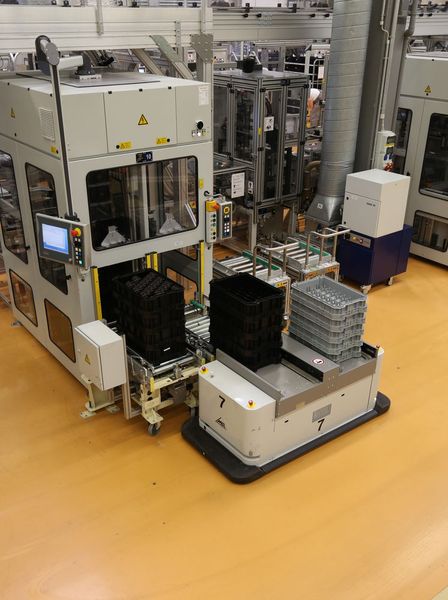 Ein fahrerloses Transportfahrzeug vom Typ Caesar übergibt Trays mit Halbfertigteilen zur weiteren Bearbeitung an eine Produktionsmaschine. (Bild: MLR Gruppe)