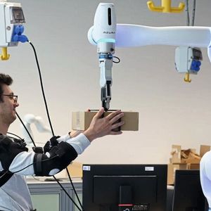 Forscher Federico Masiero nimmt ein Päckchen entgegen, dessen Gewicht der Roboter vorher bereits an das Exoskelett übermittelt hat.(Bild:  Andreas Schmitz / TUM)