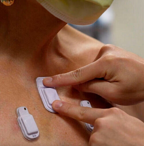 A health care worker sticks wearable devices onto an adult patient's chest. 