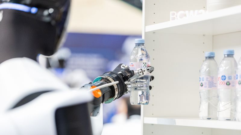 A humanoid robot takes a beverage from the shelf and places it on the counter. The demonstration at Bosch Connected World 2026 showcased key capabilities of humanoid systems in a specific handling process.(Image: Image: Schunk SE & Co. KG)