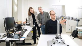 Prof. Dr. Yulia Sandamirskaya et Andreas Leu en arrière plan, tandis que Paul Fox, membre de l'équipe, présente le mouvement interactif du bras robotique avec la caméra 3D (intégrée en bas). (Source :Thomas Entzeroth)