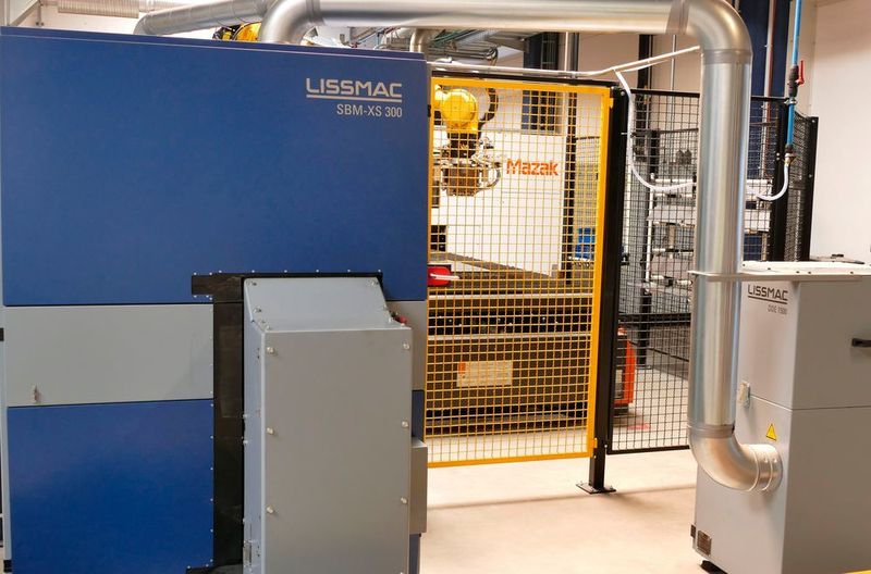 Konstellation der Klingen-Fertigungsinsel bei Gardena mit der Mazak-Laser-Flachbettanlage im Hintergrund sowie links der Entgratmaschine SBM XS 300 G1E1 und rechts daneben der Lissmac-Trockenentstauber DDE 1500 für Stahl und Edelstahl. Zwischen Mazak- und Lissmac-Anlage ist der Roboter zu erkennen. Er übernimmt innerhalb der automatisierten Fertigungszelle den Transport der Teile.  (Kuhn)