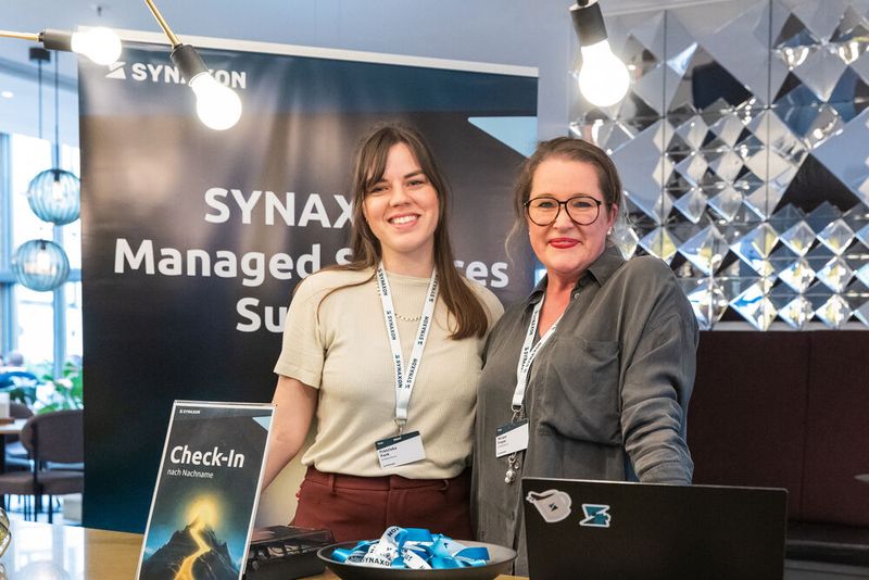 Franziska Funk und Miriam Freyer (v.l., Synaxon) begrüßen die Teilnehmenden mit einem Lächeln am Check-In. (Bild: Synaxon)