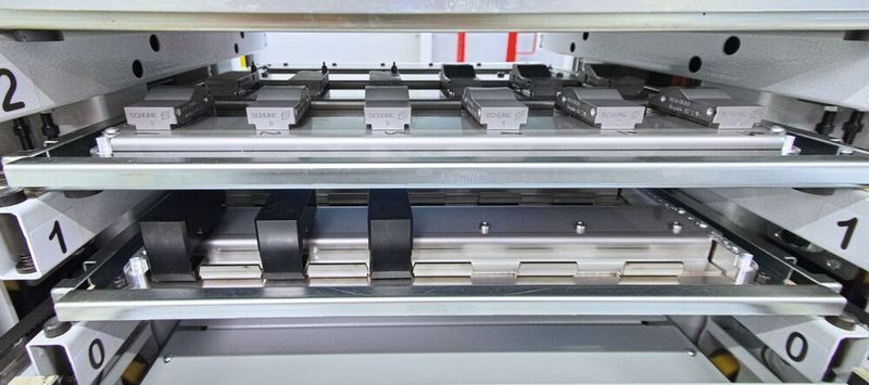 En haut de l'image, les différents mors de serrage stockés dans le système de tiroirs de la tour de stockage (objectif : 50 jeux de mors de serrage). En bas de l'image, un mors de serrage est en cours de montage automatique sur le mandrin à 3 mors de Schunk. Auparavant, les copeaux ont été automatiquement éliminés par rinçage au liquide de coupe et à l'air comprimé. (Bild: Matthias Böhm)