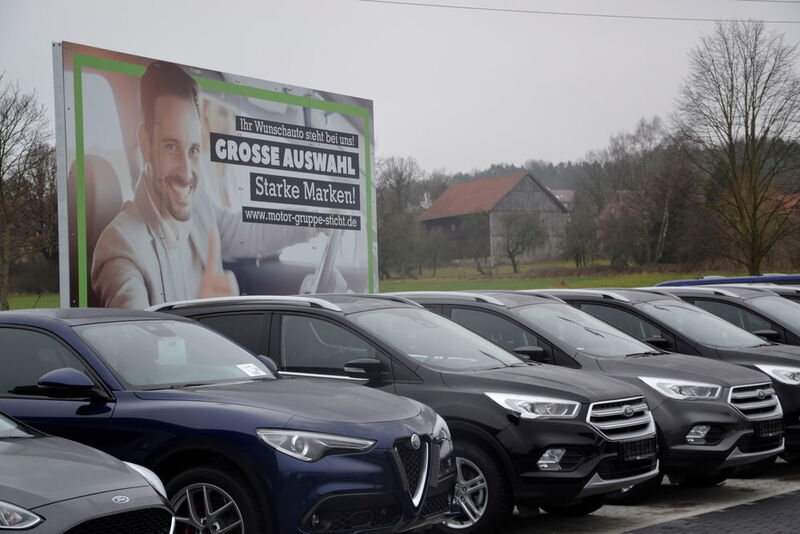 Mehrere großformatige Werbeplakate weisen die Interessenten, die auf dem  Gebrauchtwagenplatz flanieren, auf die Vorteile der MGS-Gebrauchtwagen hin. (Mauritz)