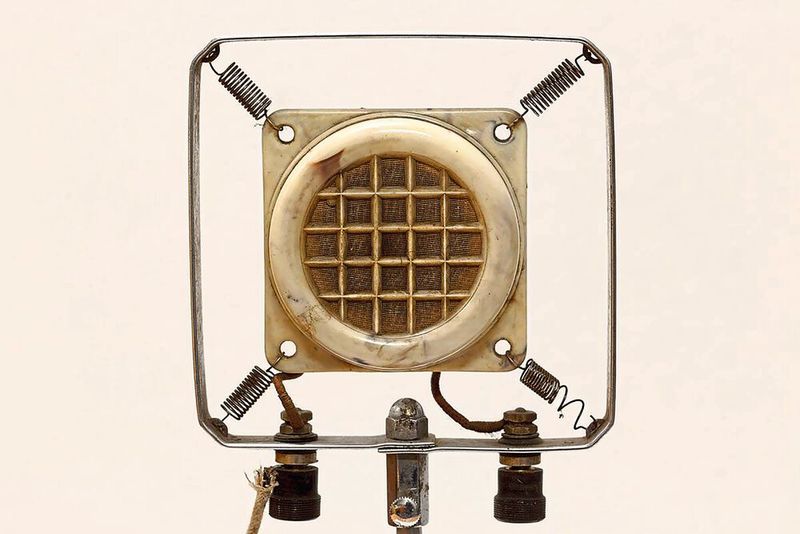 1877: Das Kohlemikrofon. Im Jahr 1877 hat Emil Berliner das erste Kohlemikrofon erfunden. Ihm schreibt man auch die Erfindung der Schallplatte und des Grammophons zu. Unabhängig voneinander entwickelte David Edward Hughes zeitgleich ein ähnliches Modell, welches auf den Grundlagen des Telefons von Reis basiert. Allerdings verzichtete er auf eine Patentierung. Durch die Erkenntnis, dass Kohle die Schwingungen einer Membran in elektrische Impulse umsetzen kann, konzentrierte man sich nun auf die Weiterentwicklung. Zur Funktion: Trifft Schall auf die Membran, drückt diese auf die Kohle, wobei die elektrischen Impulse bestehen. Kohle eignet sich besonders gut für die Leitung der Signale. Kurze Zeit später gelang der nächste Schritt. Körner aus Kohle ersetzten die bisherigen Kohlestäbe. Man stellte fest, dass damit ein noch besseres Resultat möglich ist. Es war der Engländer Henry Hunnings, der auf die Idee kam und dieses Mikrofon erfunden hat. Mit dieser Technik wurde das Kohlemikrofon bis in die 1960er Jahre genutzt. (Bild: Maximilian Schönherr / CC BY-SA 3.0)