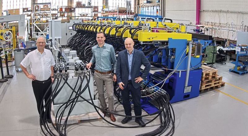Dieter Mühlethaler, Christian Schmidt und Thomas Ritter (v. l. n. r.) arbeiteten im Rahmen des Projekts eng zusammen. Links im Bild das GRIBI-Hydrauliksteuerungsaggregat, rechts im Hintergrund die Presse mit gesamthaft 40 Hydraulikzylindern. (Bild: Matthias Böhm)