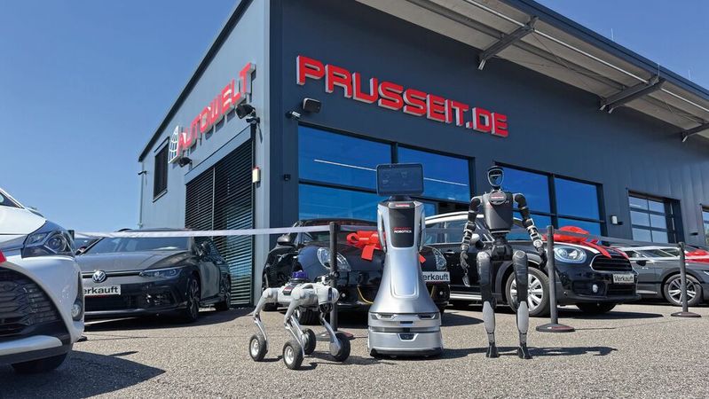 Kollaboratives Trio vor der Autowelt Prusseit in Horb am Neckar: Der rollende Orionstar-Roboter (Mitte) bildet das zentrale Nervensystem, der Quadruped von Neura Robotics (l.) kartografiert das Gelände, der Unitree-Humanoide übernimmt Botengänge wie das Holen von Fahrzeugschlüsseln.(Bild:  Achter – VCG)