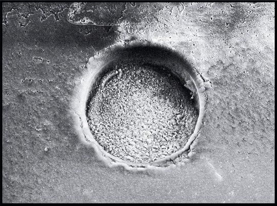 160 Mikrometer kleiner Messkrater im vulkanischen Glas: Er entsteht, wenn ein Laser winzige Mengen Material aus der Probe herausschießt. Dieses Material wird mit einem Gas in ein Massenspektrometer eingebracht, dort stark erhitzt und in seine Bestandteile zerlegt. So können Forschende genau bestimmen, welche Elemente und Isotope in der Probe enthalten sind.(Bild:  aus Garbe-Schonberg, D. and Müller, Nano-particulate pressed powder tablets for LA-ICP-MS, JAAS)