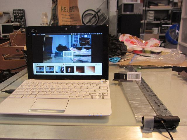 Look at a barcode through the webcam to refocus it to about 20 cm away. Use a webcam program like Photo Booth. A barcode has fine details so it's a nice test of focus. (The above image is of an older kit). Rotate the camera lens to adjust the focus. You may need to gently use a pair of needle-nosed pliers at first. Anything around 20 cm away from the lens should be in focus. This means your slit will be in focus when the box is closed. If you don't carefully refocus your camera, your spectra will be of very low resolution. Now snap your webcam back together. (Bild: PLOTS/CC BY 2.0)