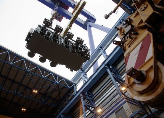 Noch in der Werft in Warnemünde werden die Transformatoren auf der Topside, dem später über dem Wasserspiegel liegenden Teil der Plattform, installiert. Wie auf dem Bild zu sehen ist, werden die Transformatoren per Kran an ihren Bestimmungsort gehoben. Die Öffnung, durch die der Trafo eingehoben wird, wird anschließend verschweißt, kann aber wieder geöffnet werden, falls ein Austausch notwendig sein sollte. Auf der Plattform BorWin2 sind neben kleineren auch zwei der großen Konverter-Transformatoren installiert. Diese wiegen je 440 Tonnen und werden im Nürnberger Transformatorenwerk von Siemens gefertigt. (Siemens AG)