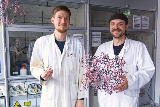 Lasse Wegner (l.) und Kalle Mertin (r.) sind Erstautoren der beiden Studien und präsentieren eine Testzelle für die Wassergewinnung und ein Modell der hochporösen Metall-organischen Gerüstverbindung (MOF), die das Forschungsteam für die Wassergewinnung aus Luft und energieeffiziente Kühlung optimiert hat. (Bild:  Christina Anders, Uni Kiel)
