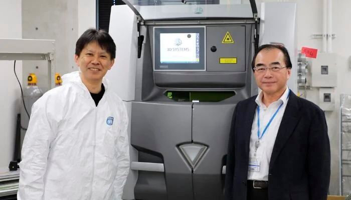 Naoki Takata von der Universität Nagoya, leitender Forscher des Projekts (links), und Masaki Kato, Hauptautor und Abteilungsleiter am Zentrum für Industrie und wissenschaftliche Technologie der Präfektur Aichi (rechts), mit dem Laser‑3D‑Drucker des Zentrums, der die Herstellung widerstandsfähigerer und hitzebeständigerer Aluminiumlegierungen ermöglicht. (Bild: Universität Nagoya)