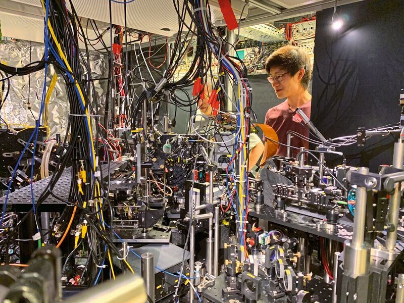 Jun Rui und David Wei, die zwei Erstautoren der Publikation, vor dem komplexen experimentellen Aufbau, in dessen Herzen sich unsichtbar der leichteste Spiegel der Welt befindet - ein Spiegel aus Atomen.