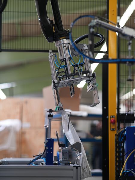 Bild a): Die Bilder a) bis e) zeigen den Transport eines Beutelstapels vom Ablageort über das Anbringen von Pappe und Stopfen sowie das Verschuppen des Bügels bis zur Ablage in den Karton. (Bild: Bihl+Wiedemann)