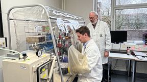 Raphael Trischler (sitzend) und Volker Müller im Labor an einer Anaerobenkammer. Diese enthält keinen Sauerstoff, sondern Stickstoff, sodass Sauerstoff-sensible Bakterien wie Blautia luti darin gefahrlos gehalten werden können. (Bild: Jennifer Roth, Goethe-Universität Frankfurt)