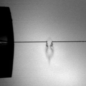 Abb. 2 Ein Infrarot-Laser trifft einen Mikroflüssigkeitsstrahl (Durchmesser etwa 10 µm; Länge des kontinuierlichen Bereichs bis der Strahl in Tröpfchen zerfällt ist etwa 1,5 bis 2 Millimeter) und setzt geladene Biomoleküle direkt aus der flüssigen wässrigen Phase frei für eine Massenanalyse.  Bild: Aufnahme mit einer Hochgeschwindigkeitskamera in Kooperation mit Dr. B. Stasicki, DLR Göttingen