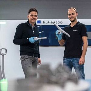 Applikationsentwickler Chris Lengwenat (re.) und sein Kollege Nicolas Haydt, Technologieexperte Additive Manufacturing beim Maschinenhersteller Trumpf, präsentieren den im 3D-Druck aus Aluminium hergestellten Fahrradlenker.(Bild:  Trumpf)