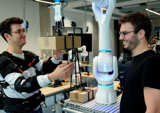 Federico Masiero (li. mit Exoskelett) und Emanuele Aimi testen die Zusammenarbeit mit einem Roboter von Neura Robotics. (Bild:  Andreas Schmitz / TUM)
