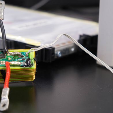 Die grüne Platine enthält den elektronischen Schaltkreis, mit dem die Forschenden Sensordaten über die vorhandenen Stromanschlüsse einer Batteriezelle übertragen. Die Batteriezelle befindet sich im Hintergrund. (Bild: Christina Anders, Uni Kiel)