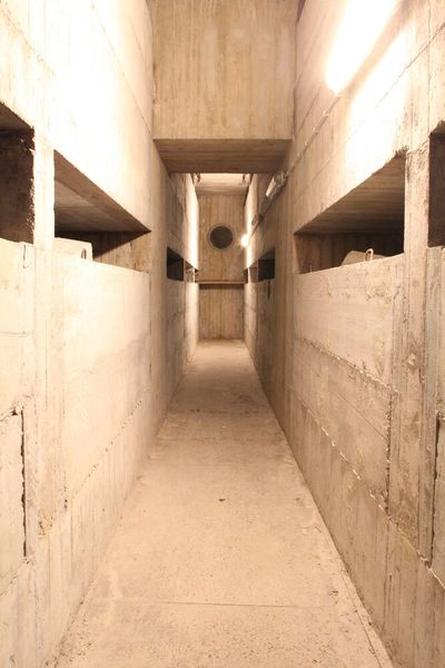 Im Untergeschoss des Bunkers - Der Bunker gleicht einem Schiffsrumpf: Die oberen Stockwerke sind gleich lang und breit. Doch nach unten verjüngt sich die Form. Obwohl sowohl die Innen- als auch die Außenwände 3 Meter dick sind und aus Strahlungssicherem Beton besteht, die Decke immerhin 6 Meter stark ist, sollte sich der gesamte Bau bei einem Atomangriff der Druckwelle standhalten und reagieren wie ein Schiff bei Wellengang; denn er ist in Kies gelagert und wäre mit Einschränkung beweglich, so dass die Schockwelle ein Kippen und Wiederaufrichten bewirkt hätte.  (Bild: Comback)