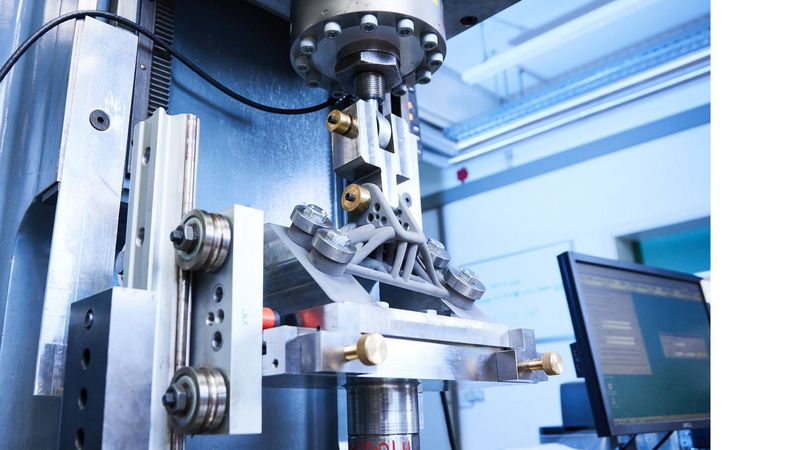 Zyklische Belastungsprüfung eines additiv gefertigten Metallbauteils nach einer mechanischen Oberflächenbehandlung an den hochbeanspruchten Zonen. Im Versuch wird der Lebensdauergewinn durch die Nachbehandlung getestet.(Bild:  Fraunhofer IWM/Kai Wudtke)