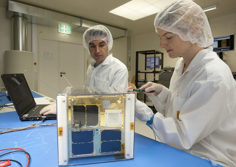 Manuela Unterberger (r) und Patrick Romano (l) mit TUGSAT-1 im Reinraum an der TU Graz. (TU Graz/Lunghammer)