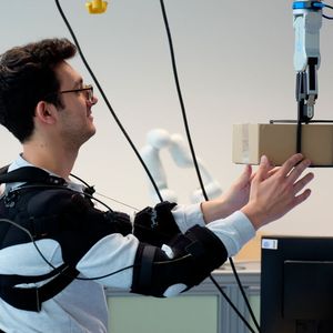 Forscher Federico Masiero nimmt ein Päckchen von einem Roboter (von Neura Robotics) entgegen. (Bild:  Andreas Schmitz / TUM)