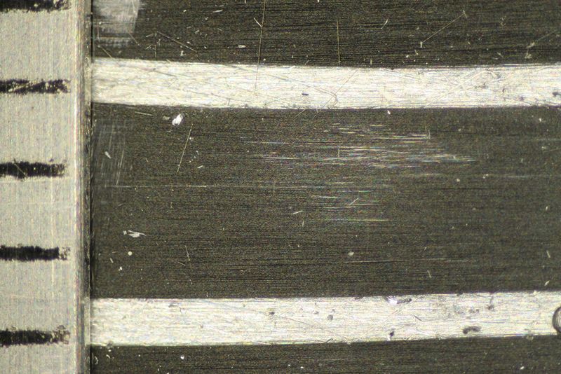 Spliss bei Versagen: CFK-Hybridwerkstoff im Lichtmikroskop neben einer Millimeterskala (links) vor und (rechts) nach dem Versagen im Zugversuch – Faserverlauf von links nach rechts [1]. Beim Versagen spleißen die Faserbündel auf und die Matrix ist quer und längs der Faserrichtung gerissen. (Beuth Hochschule)