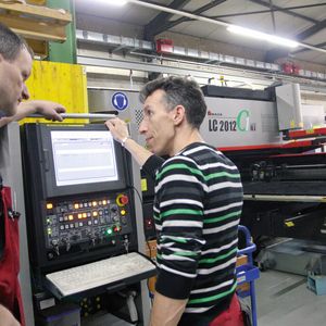 Geschäftsführer Marcel Wüst (links) im Gespräch mit einem Mitarbeiter an der Maschinensteuerung der Amada LC-2012 C1.