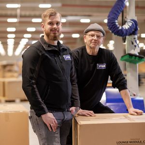 Rückenscherzen ausgemerzt! Von links: Bastian Böhm, Operations Manager bei JYSK, und Hans-Christian Hessler, dort Schwerbehindertenvertreter, im Homberger Logistiklager der JYSK Group. Rechst daneben der Vakuumschlauchheber Jumboflex Picker von Schmalz, der dort nun die Körperkräfte der Mitarbeiter schont.(Bild:  Schmalz / M. Wagenhan)