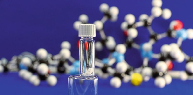 Im Labor synthetisiertes Lugdunin, im Hintergrund das Strukturmodell. (Universität Tübingen, Sebastian N. Wirtz)