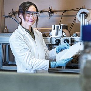 Zhenzhen Zhang präsentiert die Herstellung der Membran mit der institutseigenen Membranziehmaschine (im Hintergrund)(Bild:  HZG/Steffen Niemann)