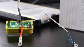 Die grüne Platine enthält den elektronischen Schaltkreis, mit dem die Forschenden Sensordaten über die vorhandenen Stromanschlüsse einer Batteriezelle übertragen. Die Batteriezelle befindet sich im Hintergrund. (Bild: Christina Anders, Uni Kiel)